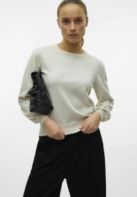 Pull en tricot gris clair avec un col rond, des manches longues froncées et des poignets à bords scallopés, assorti à un sac en cuir noir.