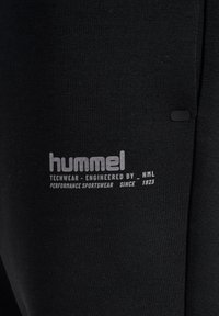 Sort stof med hvid tekst, der lyder "hummel, techwear engineered by HML, performance sportswear since 1923".