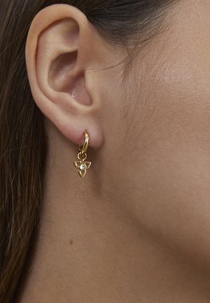 Left ear with a small gold hoop earring featuring a delicate three-petal flower charm with a central pearl detail.