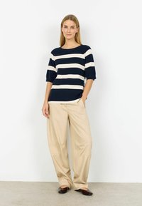 Tumši zils un krēmkrāsas svītrains adīts tops ar apaļu kaklu un īsām piedurknēm, kopā ar bēšām platām biksēm un tumši brūnām dzīvokļkurpēm.