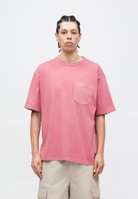 Ροζ βαμβακερό t-shirt με στρογγυλή λαιμόκοψη, κοντά μανίκια και τσέπη στο αριστερό στήθος. Το ρούχο έχει άνετη εφαρμογή και λεπτή υφή.