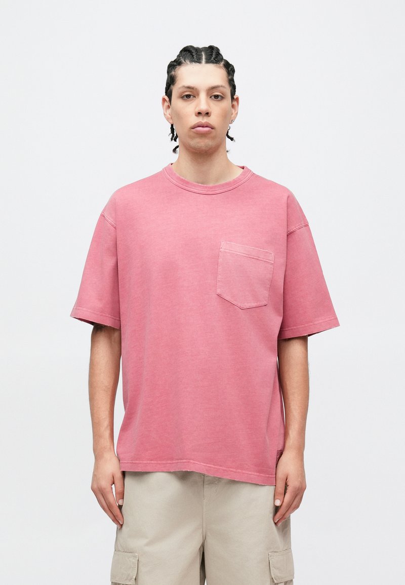 Lyserød bomuld T-shirt med rund halsudskæring, korte ærmer og en brystlomme på venstre side. Tøjet har en afslappet pasform og en subtil tekstur.