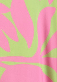 Tela verde brillante con grandes formas de hojas abstractas en color rosa superpuestas, mostrando una textura suave y ligeras arrugas en la tela.