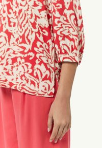 Czerwona i biała bluzka w wzory z rękawami o długości trzech kwart, charakteryzująca się luźnym krojem i bocznymi rozcięciami, zestawiona z jednolitymi spodniami w kolorze koralowym.
