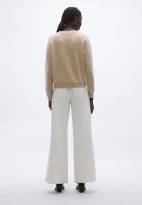 Beżowy, miękki sweter z długimi rękawami, zestawiony z białymi spodniami o szerokich nogawkach, posiadającymi tylne kieszenie i czysty brzeg. Brązowe buty na obcasie.