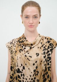 Top de estampado de leopardo hecho de una tela suave; cuenta con escote drapeado, mangas cortas y una mezcla de tonos beige y marrón con manchas negras.