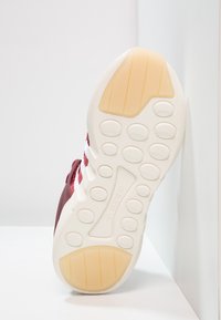 Červená sportovní bota s texturovaným svrškem a bílým designem tří pruhů. Disponuje gumovou podrážkou s kruhovými gripy a hladkým mezipodešvem.