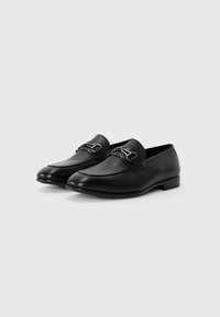 Mocassins en cuir noir avec une finition lisse, dotés d'une boucle en métal décorative et d'un talon bas. Design à bout rond avec un détail de texture subtil.