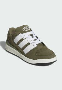 Olive green sneakers with white leather stripes, padded tongue, and textured fabric. Features a rubber sole with a contrasting black outsole.