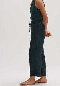 Mörkgröna linbyxor med avslappnad passform, elastisk midja och snörningsdetalj. Stylistiskt kombinerade med en åtsittande stickad topp och platta sandaler.