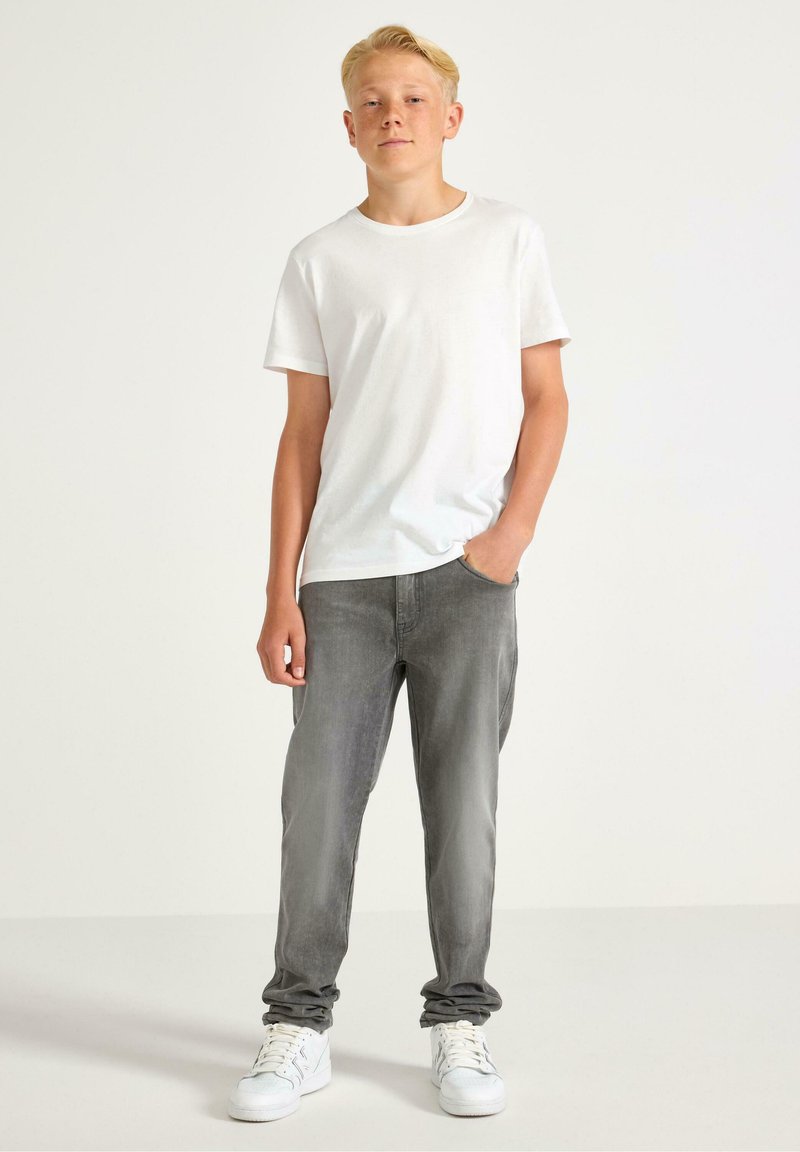 Witte katoenen T-shirt gecombineerd met grijze spijkerbroek. De spijkerbroek heeft een slim fit en een lichte vervaging. Witte sneakers maken de outfit compleet.