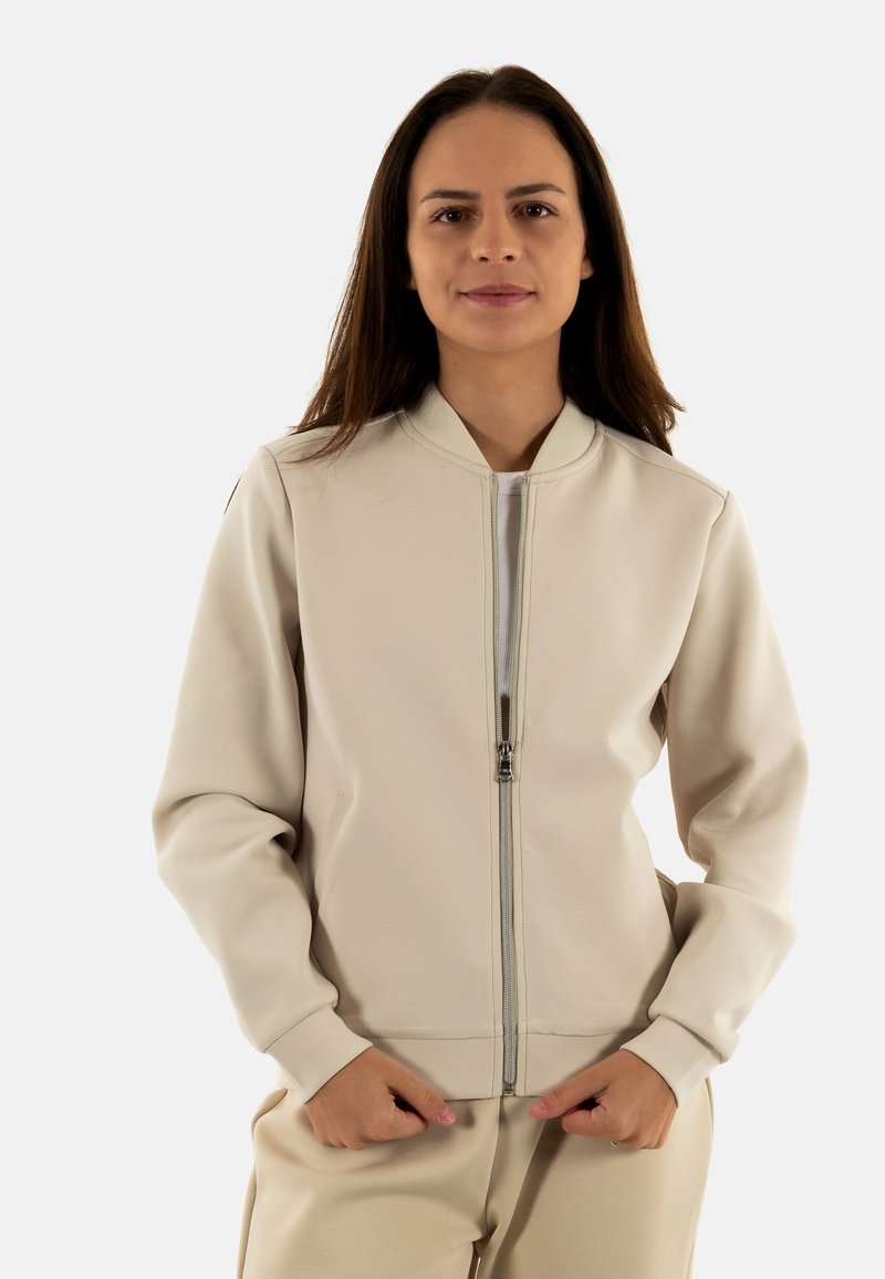 Giacca zip-up beige chiaro con colletto alto, polsini a coste e tasche laterali, realizzata in un tessuto morbido.