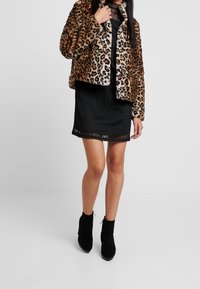 Leopardprint faux fur jakke, sort ribbet kjole med gennemsigtig kant, parret med sorte ankelstøvler. Teksturerede stoffer og dyremønsterdetaljer.