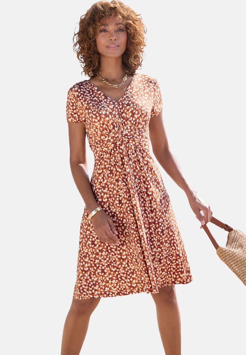 Braunes Blumenkleid mit V-Ausschnitt, kurzen Ärmeln und tailliertem Schnitt. Hergestellt aus leichtem Stoff mit einem fließenden Rock. Geflochtene Tasche als Accessoire.