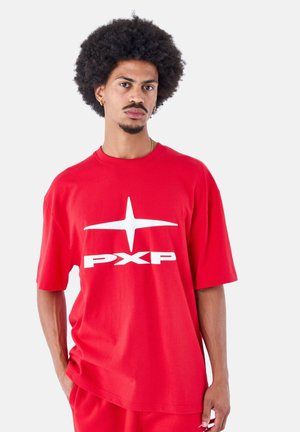 Camiseta de algodón roja de gran tamaño con mangas cortas y un logotipo blanco "PXP". Textura suave y diseño simple. Combinada con unos pantalones rojos a juego.