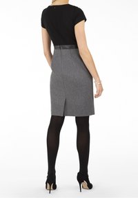 Haut noir à manches courtes et jupe grise, avec un accent en cuir à la taille et une fente au dos. Porté avec des collants noirs et des talons.