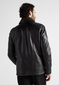 Schwarze Lederjacke mit strukturiertem Finish, ausgestattet mit einem fellartigen Kragen und Rückennahtdetails. Keine sichtbaren Hardwareakzenten.