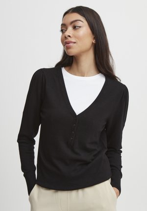 Black long-sleeve top with a V-neck, featuring button accents and ribbed cuffs. Worn over a white t-shirt, it has a soft texture.
