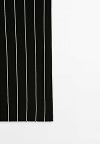 Tissu noir avec fines rayures blanches verticales sur un fond gris clair, montrant un gros plan du bord.