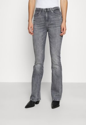 Personne portant un jean gris taille haute, droit, délavé, avec des bottines noires à bout pointu et un haut blanc sans manches.