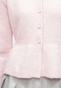 Jasnoróżowy kardigan z fakturowanym dołem i pięcioma ozdobnymi guzikami przypominającymi perły, wykonany z miękkiego dzianinowego materiału.
