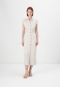 Robe en lin beige à boutons avec des manches courtes à empiècement, des fentes sur les côtés et une taille ajustée, associée à des sandales à lanières brun clair.