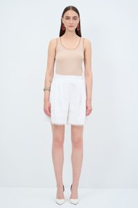 Top sin mangas beige con cuello redondo y ribete naranja; pantalones cortos blancos con bordado floral y dobladillo de puntilla con forma de concha; combinado con tacones blancos.