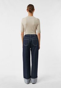 Beżowy top z krótkim rękawem w połączeniu z ciemnoniebieskimi szerokimi spodniami jeansowymi z podwiniętymi nogawkami i dwoma tylnymi kieszeniami z białym przeszyciem.