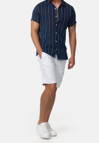 Niebieska koszula z krótkim rękawem w pionowe białe i złote paski, połączona z białymi szortami z teksturowymi akcentami i białymi trampkami.