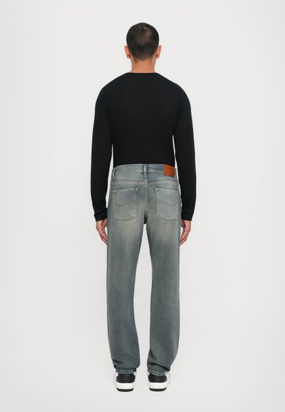 Blue denim jeans with a straight cut, light wash, and subtle fading, paired with a black long-sleeve shirt and black-and-white sneakers.