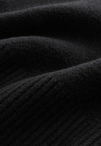 Puha fekete kötött anyag bordás mintával, közelről látható hajtásokkal és textúra részletekkel.