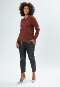 Maglione a maglia marrone con motivo a diamante, abbinato a pantaloni in ecopelle neri e scarpe con tacco alto glitter argento. Silhouette casual e aderente.