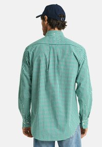 Groen- en wit-geruite blouse met lange mouwen van katoen, met een button-down kraag en een gebogen zoom ter hoogte van de heup, gedragen met een marineblauwe pet.