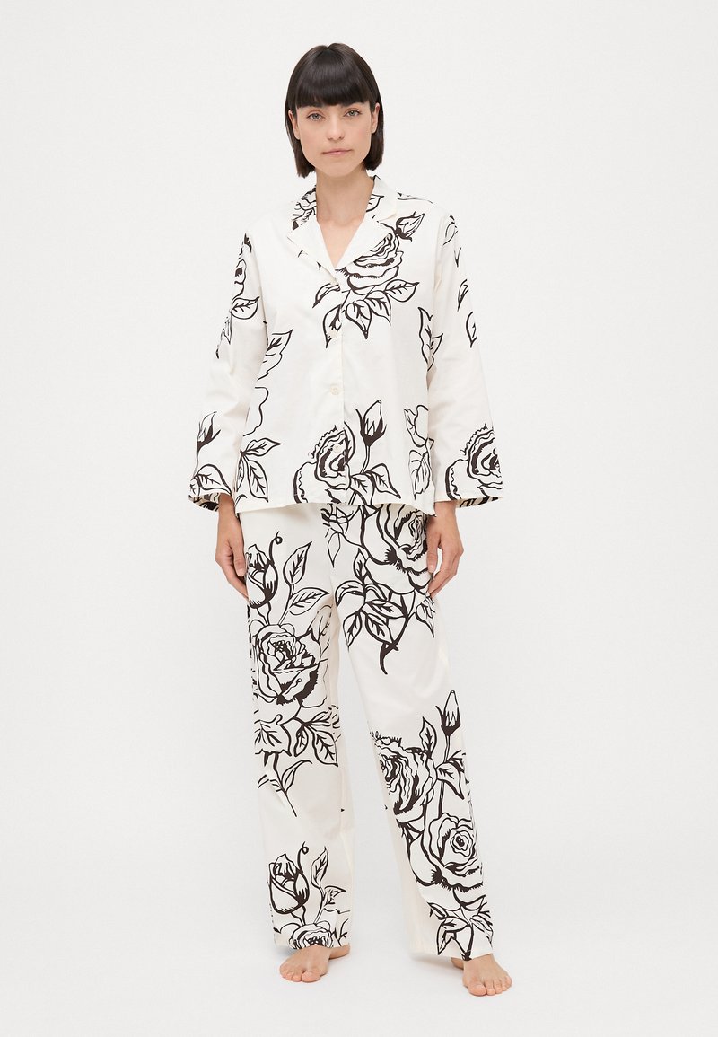 Set de pijamale alb cu imprimeu floral negru. Cămașa are guler și închidere cu nasturi; pantalonii sunt lejeri, având un model similar.