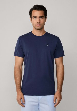 Marineblaue Baumwoll-T-Shirt mit kurzen Ärmeln, Rundhalsausschnitt und einem kleinen weißen Logo auf der linken Brust. Glatte Textur und normale Passform.