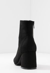 Stivale alla caviglia in suede nero con punta arrotondata, tacco spesso e chiusura con zip sul retro. Texture liscia e design senza cuciture.