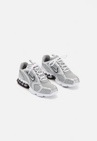 Paire de chaussures de sport en mesh argent et gris avec lacets blancs et semelles rembourrées, présentée sur fond blanc.