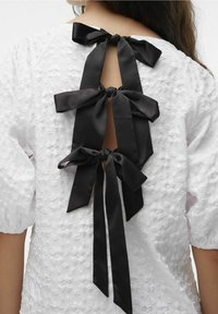 Valkoinen teksturoitu mekko, jossa on kolme mustaa satiinikaari takana, avaimenreikäaukko ja puffihihat lisäyksinä.