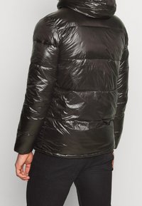 Veste matelassée noire à finition brillante, dotée d'une capuche, de manches longues et de détails de couture horizontale sur le corps.