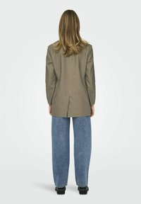 Blazer oversize grigio chiaro con spacco sul retro, abbinato a jeans di denim blu larghi, visto da dietro. Texture liscia e design strutturato.