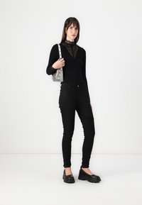 Čierne top s dlhými rukávmi s čipkovými detailmi, v kombinácii s čiernymi slim-fit džínsami s rebrovanými detailmi a čiernymi platformovými topánkami. Strieborná kabelka.