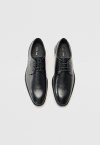 Des chaussures en cuir noir présentent une finition lisse avec une texture subtile, un bout rond, un design à lacets et des accents de couture minimaux.