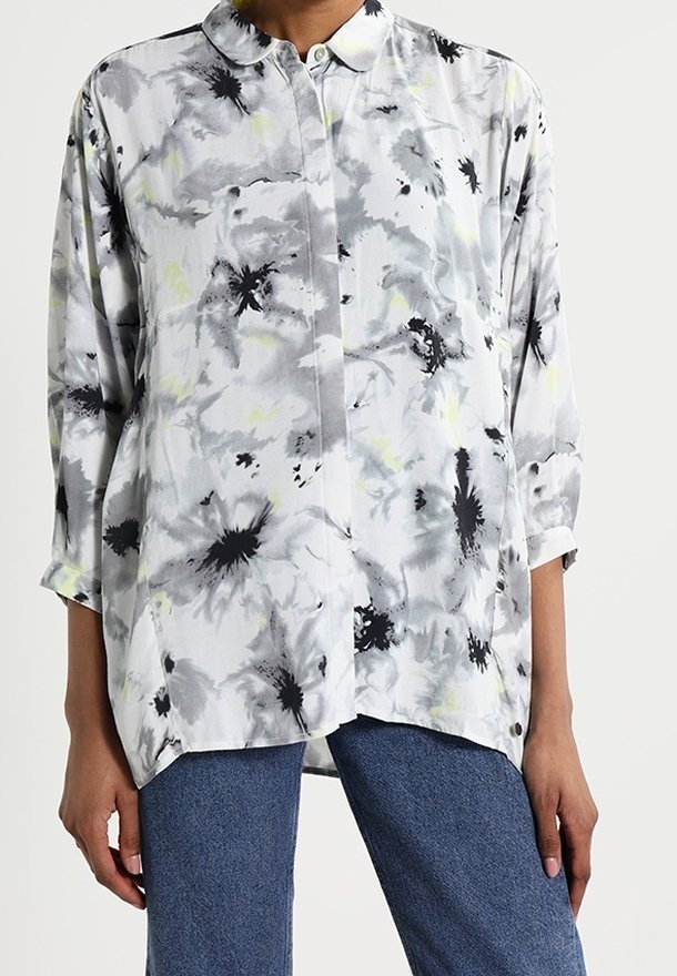 Chemise à manches longues boutonnée avec motif floral abstrait noir et gris portée avec un jean bleu, montrée des épaules aux hanches.