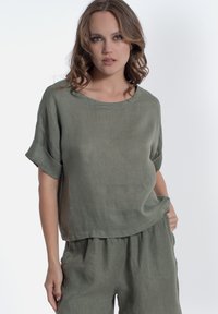 Top in lino verde oliva a maniche corte con scollo rotondo e vestibilità rilassata, abbinato a pantaloni leggeri coordinati. Texture liscia e design informale.