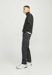 Sudadera negra con cremallera en el cuello y mangas largas, combinada con jeans de mezclilla oscura y zapatillas deportivas de color claro. Diseño sencillo y moderno.
