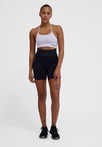 Zwarte high-waisted shorts gecombineerd met een lichtgrijze sportbeha met dunne bandjes. Het materiaal lijkt rekbaar met een gladde textuur.