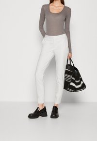 Kvinna i grå långärmad tröja, vita skräddarsydda byxor, svarta klackade loafers, hållande en stor svartvit randig tote-väska.