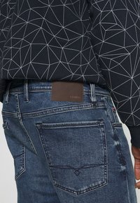 Black sweater with white geometric pattern paired with blue denim jeans featuring a brown leather label on the waistband.