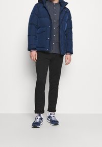 Giacca puffer blu navy con cappuccio, pantaloni neri, camicia a pois e scarpe sportive blu navy con dettagli bianchi. Texture liscia, design trapuntato.