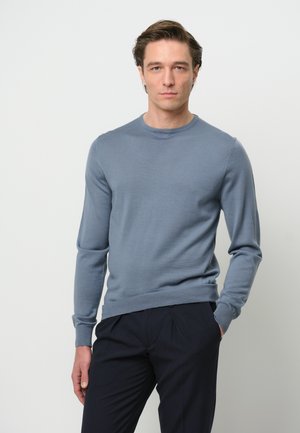 Maglione azzurro chiaro a girocollo in morbido materiale a maglia, con maniche lunghe e una silhouette aderente, abbinato a pantaloni scuri.